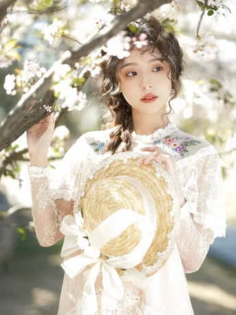 一位穿着白色和服的美女 手里拿着一顶草帽 站在盛开的花树下。