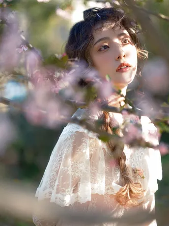 一位穿着白色连衣裙的年轻女子站在开满粉色花朵的树旁