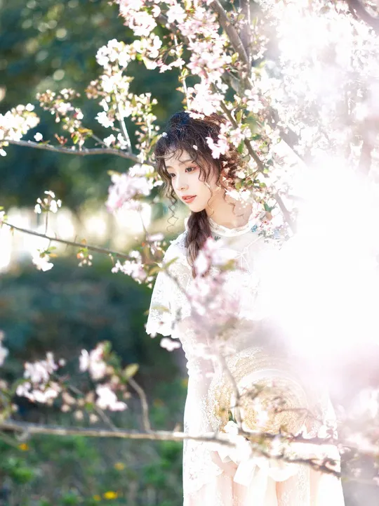 一位美丽的年轻女子穿着白色裙子站在一朵盛开的树下