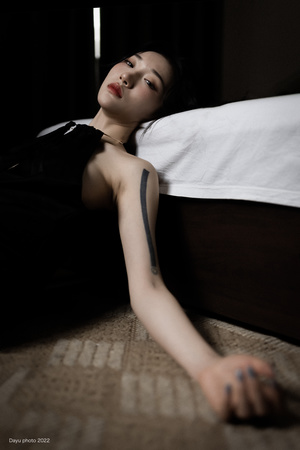 一个穿着黑色连衣裙的年轻女子躺在一个有床的房间里的地板上