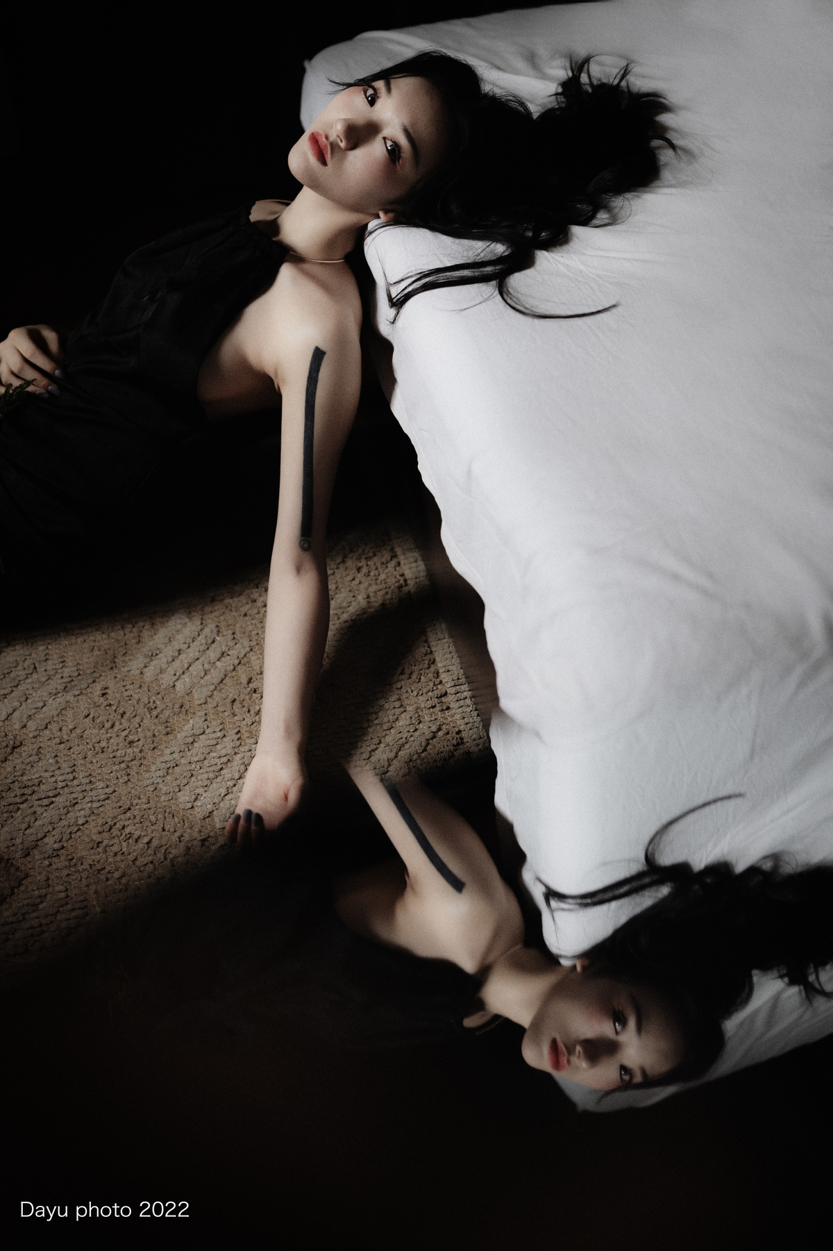 一个穿着黑色衣服的年轻女人躺在铺着白色床单和枕头的床上