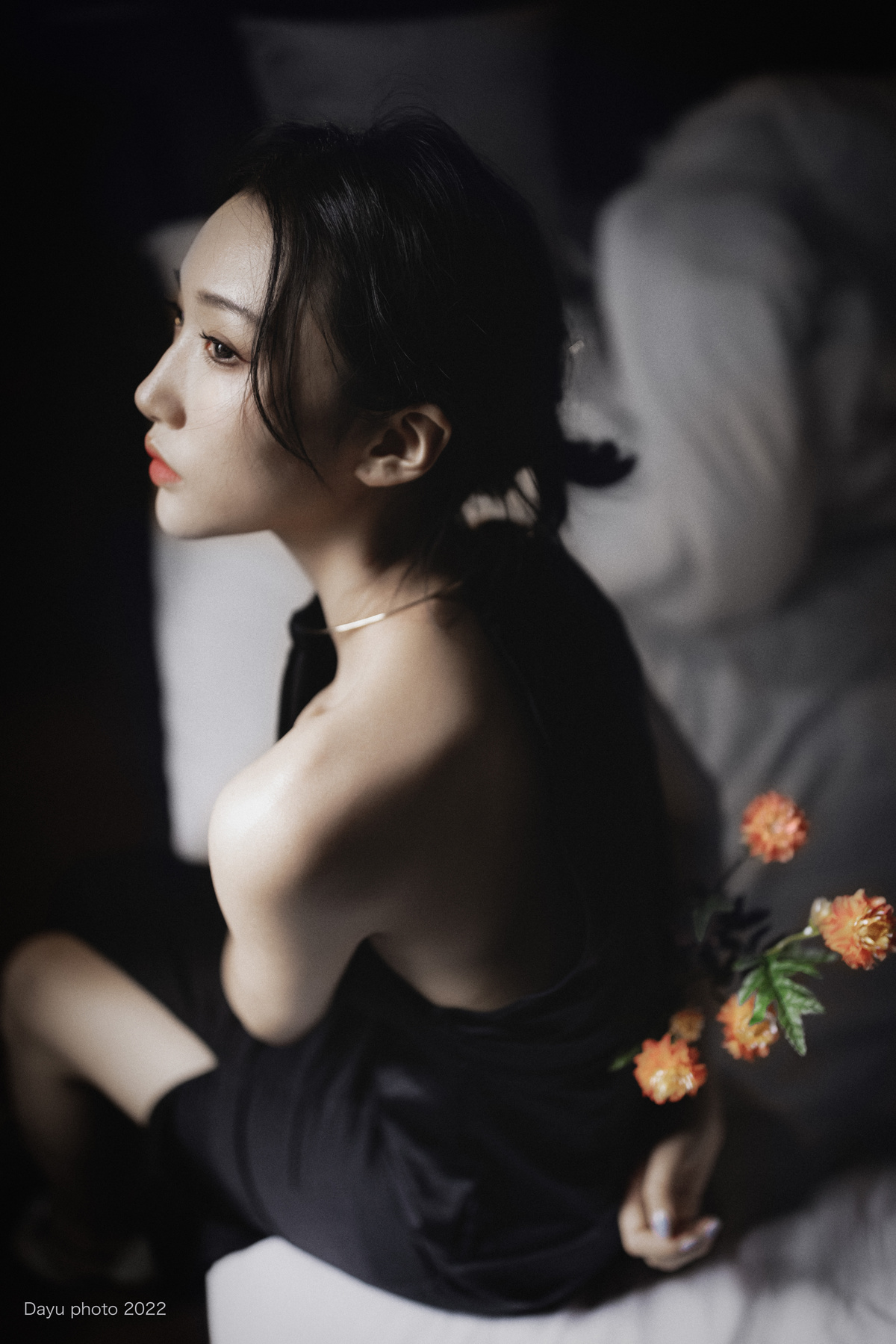 一个穿着黑色连衣裙的年轻女子坐在摆满鲜花的床上