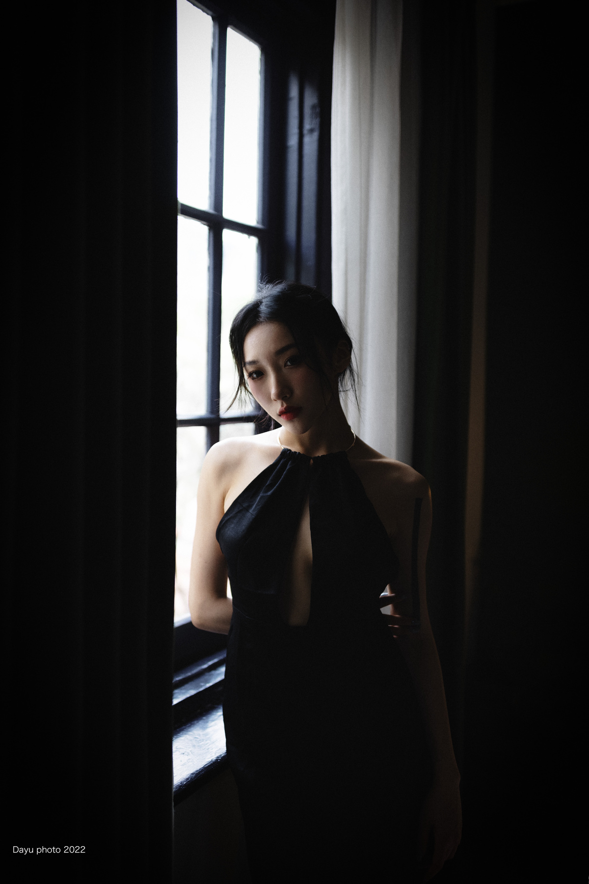 一个穿着黑色连衣裙的年轻女子站在黑暗的房间里