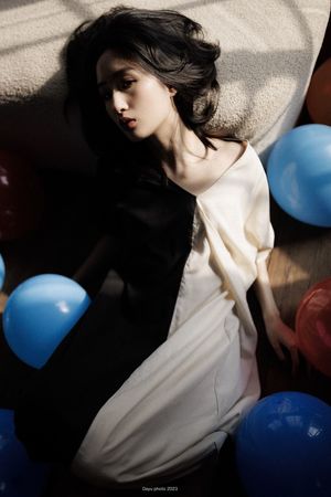 一个穿着白色连衣裙的年轻女子被蓝色气球围绕在地板上