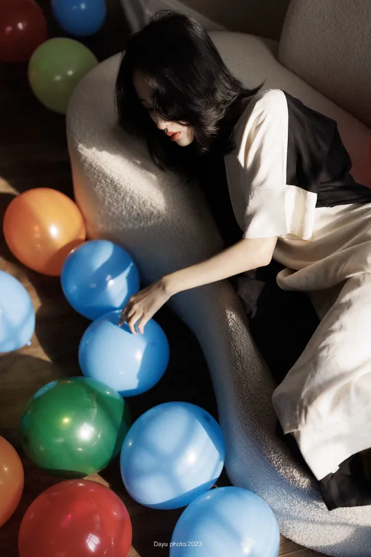 一个年轻女子坐在气球环绕的椅子上