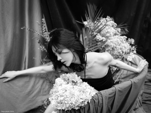 一张黑白照片 一位穿着黑色连衣裙的女士抱着一束花。