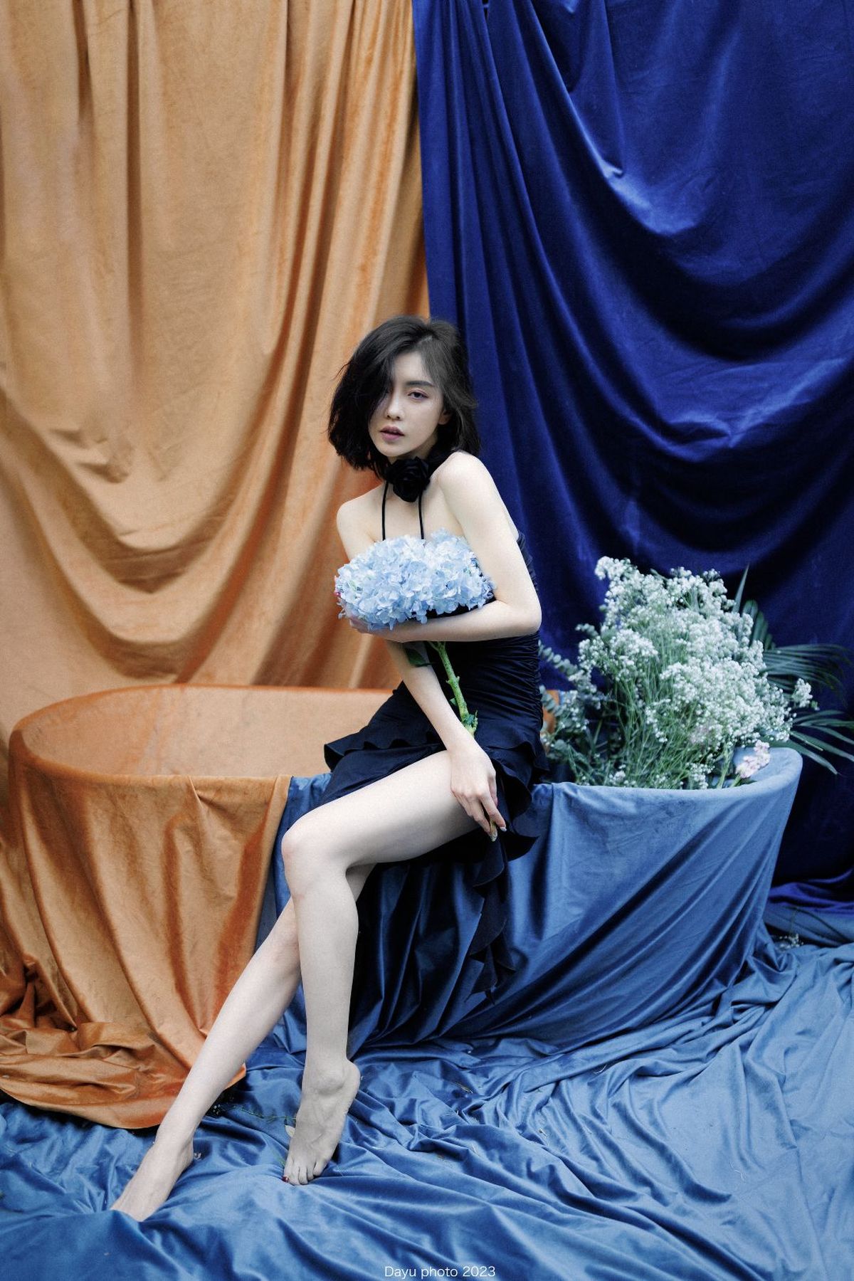一个穿着黑色连衣裙的女人 双腿交叉坐着 手里拿着一束蓝色花。