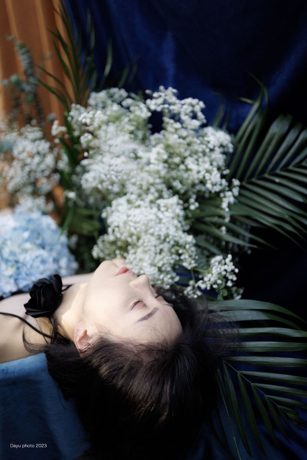 一位年轻女子躺在花束旁边 花束放在一个蓝色的花瓶里。