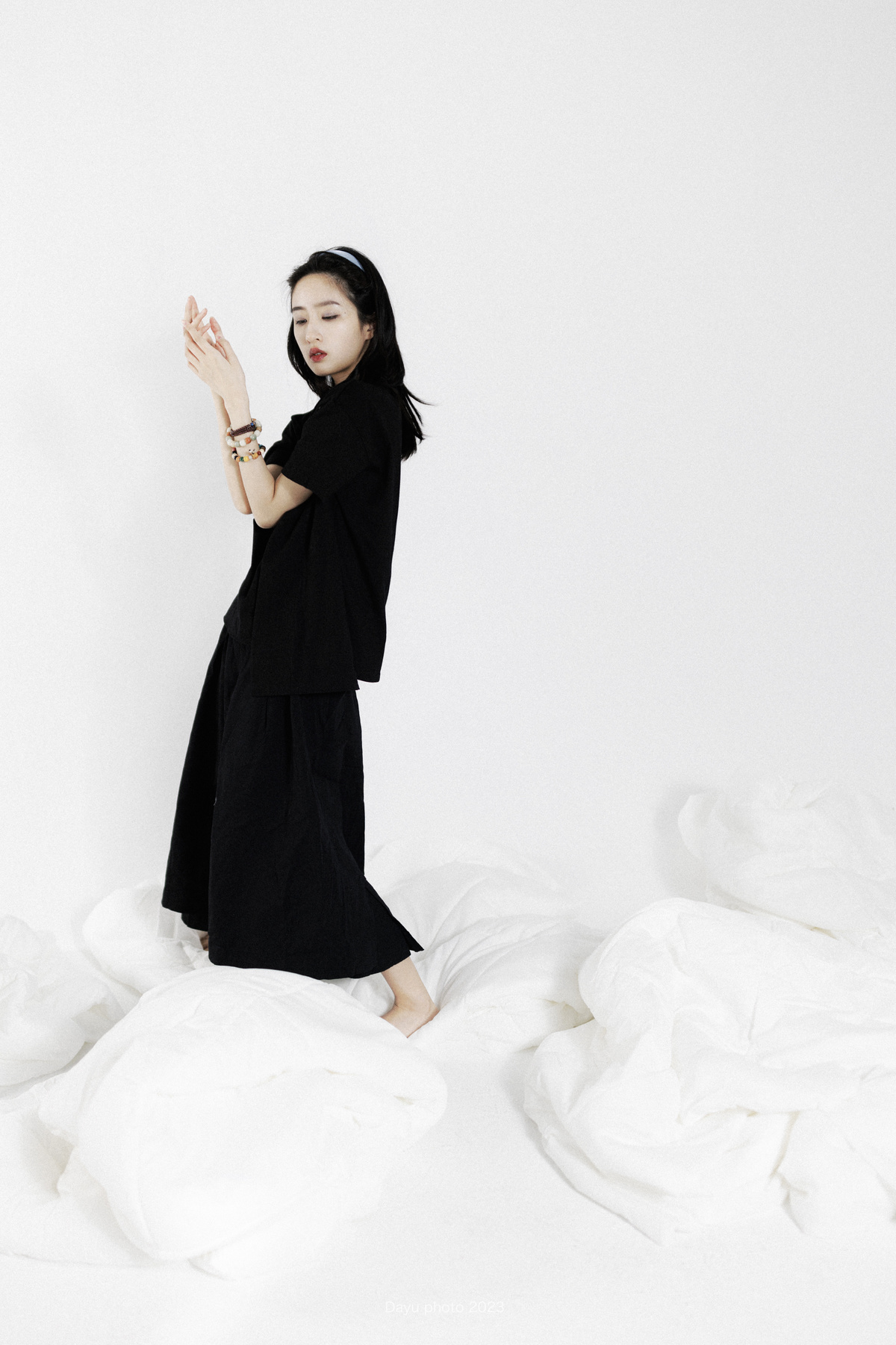一个穿着黑色连衣裙的女孩站在一张带有白色床单的床上