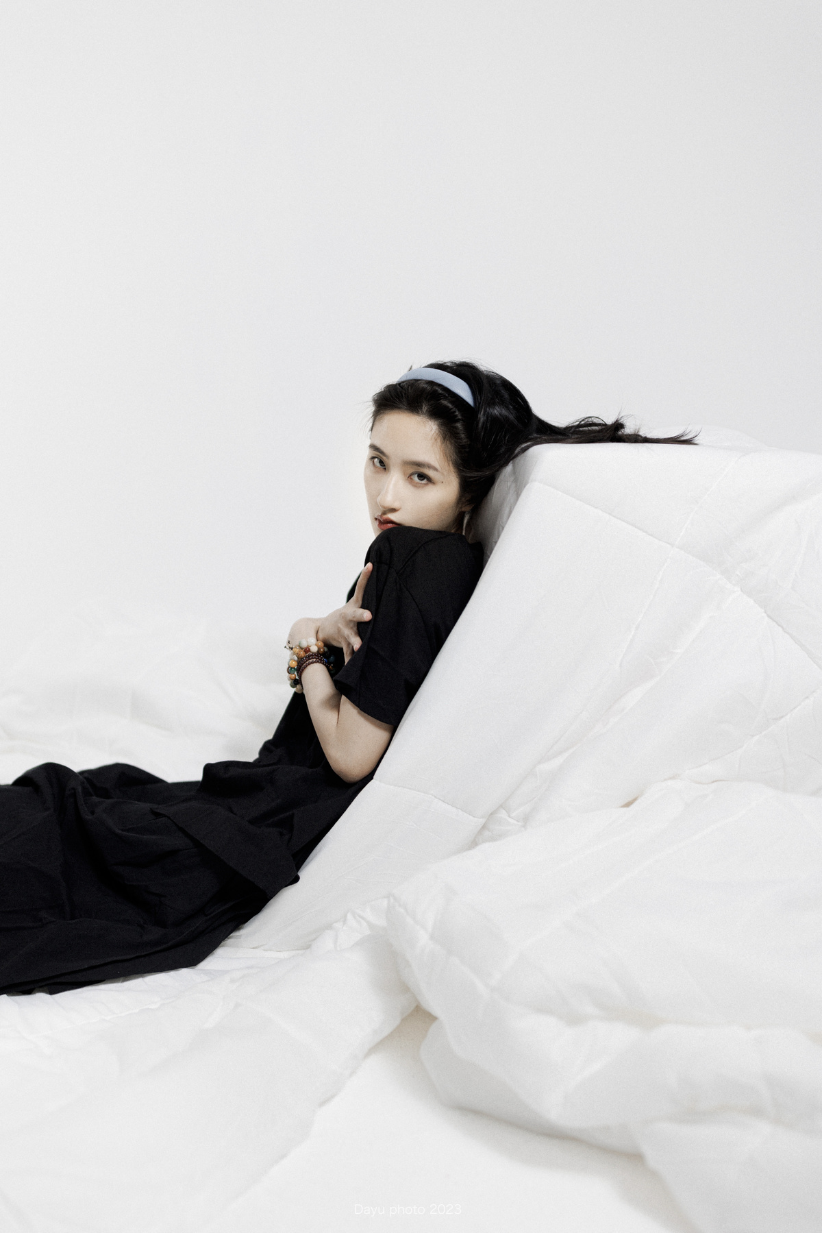 一个穿着黑白条纹的年轻女子躺在床上 身上盖着白色的床单和毯子 毯子盖在她的嘴上。