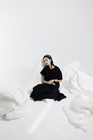 一个穿着黑色衣服的女人坐在床上有白色床单的床上