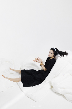 一个穿着黑色连衣裙的女人躺在铺有白色床单的床上