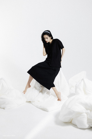 一个穿着黑色连衣裙的模特站在一张白色床上