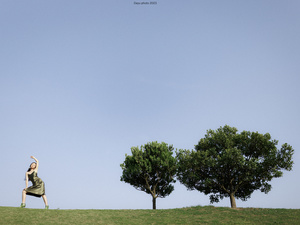 一个男人和一个女人站在一个绿草山坡上 有树木和一只风筝在天空中飞翔。