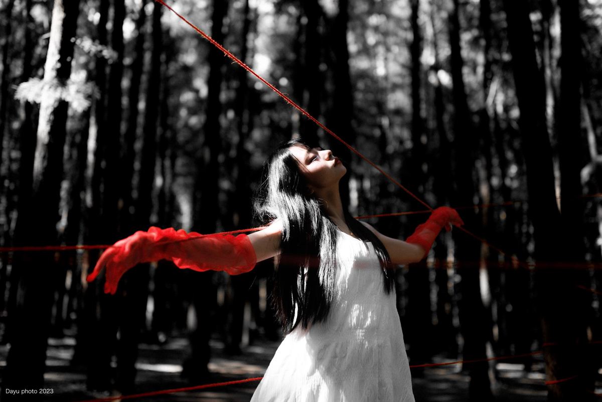 一位穿着白色连衣裙的年轻女子 手持红色雨伞 在森林中放风筝。