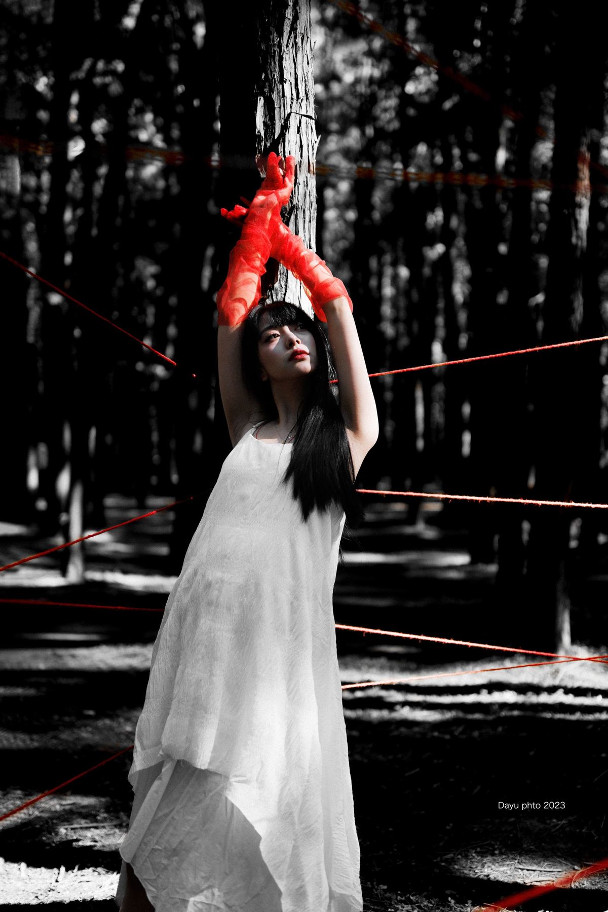 一位穿着白色连衣裙的女人举着一把红色雨伞 站在森林中 头上绕着绳子。