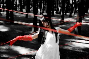 一位穿着白色连衣裙 拿着红色雨伞穿过森林的女人