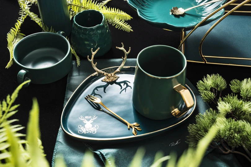 一个黑色的桌子 上面放着绿色的植物、盘子和杯子。