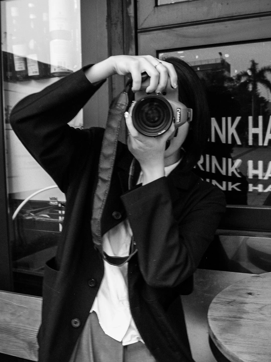 一张黑白照片 一位年轻女子手持相机 在餐厅窗户前自拍