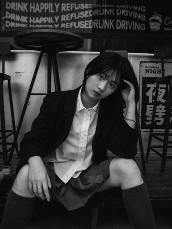 一张黑白照片 一位年轻女子穿着西装和领带坐在长椅上。