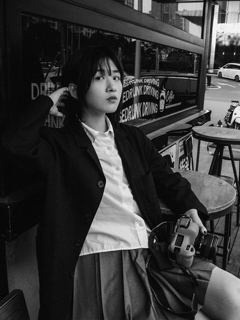 一张黑白照片 一位年轻女子坐在咖啡馆前的长凳上 面前的桌子上有咖啡。