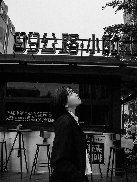 一张黑白照片 一位年轻女子走在街道上 餐厅前面有招牌。