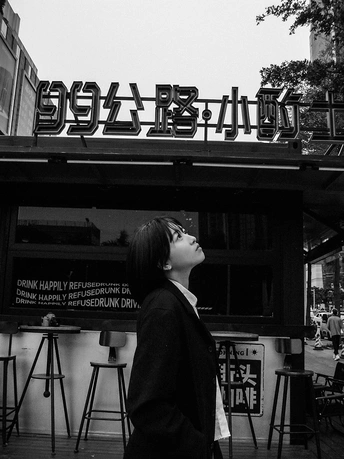 一张黑白照片 一位年轻女子走在街道上 餐厅前面有招牌。