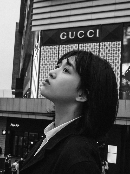 一张黑白照片 一位年轻女士站在一栋建筑前 抬头向上看。