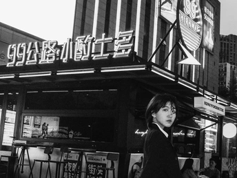 一张黑白照片 一位年轻女子正在城市的一条街道上行走。