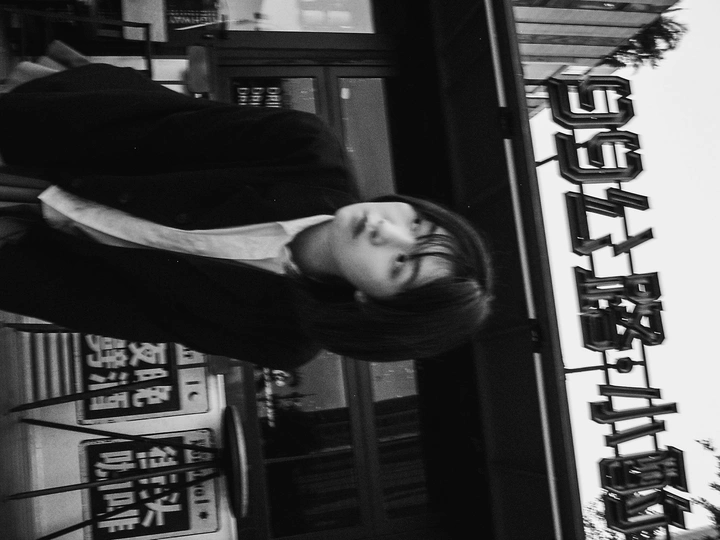 一张黑白照片 一位年轻女子站在一家名为寿司酒吧和餐厅的建筑前。