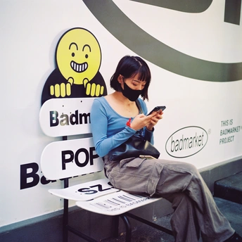 一个年轻女子坐在长凳上 正在看她的手机 手机屏幕上显示着笑脸图案 墙上有笑脸图案。