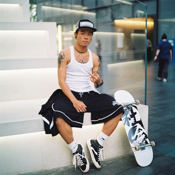 一个年轻人坐在长凳上 身边放着一些滑板。