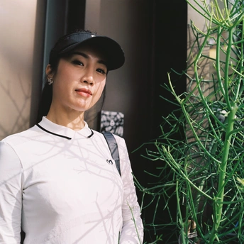 一位戴黑色帽子、站在有绿色植物的建筑前面的年轻女子