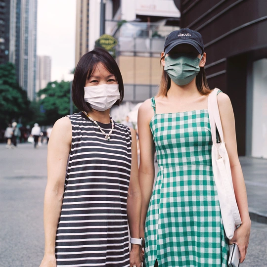 两个戴口罩的年轻女性走在城市的一条街道上。