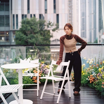 一个年轻女子站在阳台上 桌子和伞在旁边。