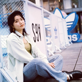 一位年轻女子坐在人行道旁的一张长椅上 旁边有一块白色的标志牌。