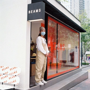 一位戴面罩的女人站在商店窗户外面 一位男子站在商店外面。