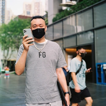 一个戴口罩的男子用手机拍照 另一个男子走在街上。