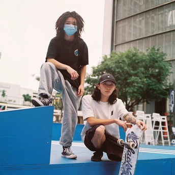 一个年轻男孩坐在长凳上 手里拿着滑板 一个妇女站在他身后 站在墙上。