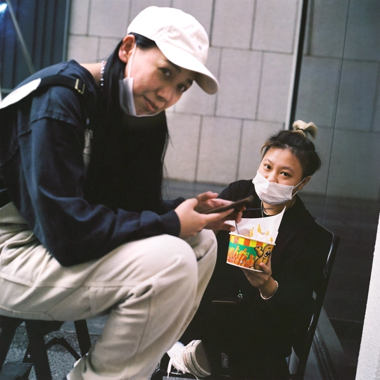 一个戴着面具的小女孩旁边坐着一个男人 手里拿着一个食物盒子。