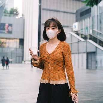 一个戴面罩的年轻女子手拿一个杯子走在街上