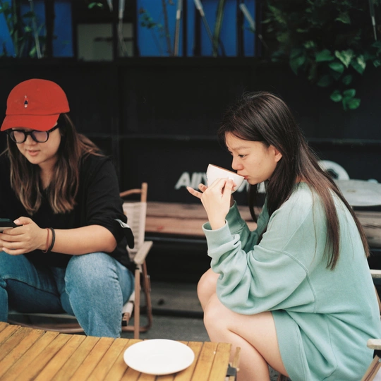 几个年轻人坐在木制桌子旁喝咖啡 并查看他们的手机。