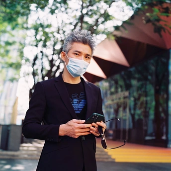 一个戴口罩的年轻人站在街上看着手机