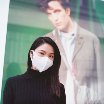 一位年轻女子戴着口罩站在广告牌前