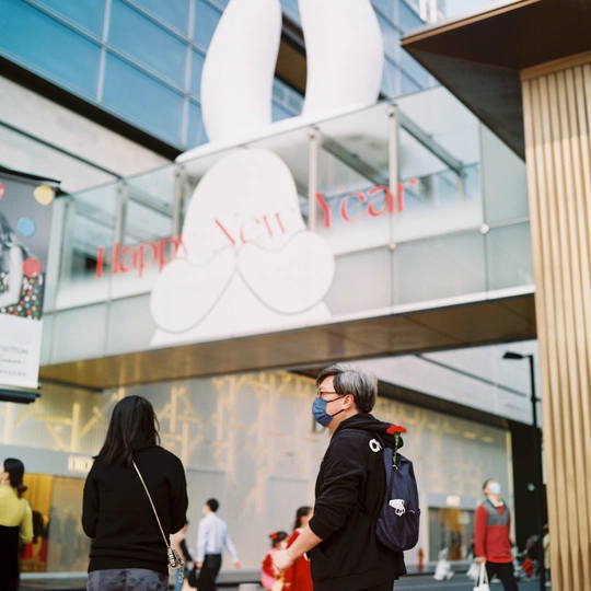 一个戴口罩的男子推着行李走在街上 前面有一栋建筑。