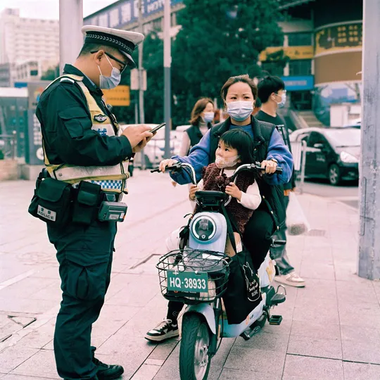 一名戴面具的警察站在一名骑滑板车的女子旁边 一名警察站在她身后 一名摩托车手在后面。