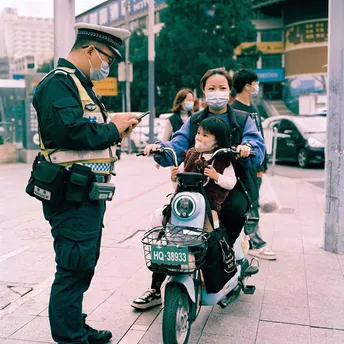 一名戴面具的警察站在一名骑滑板车的女子旁边 一名警察站在她身后 一名摩托车手在后面。