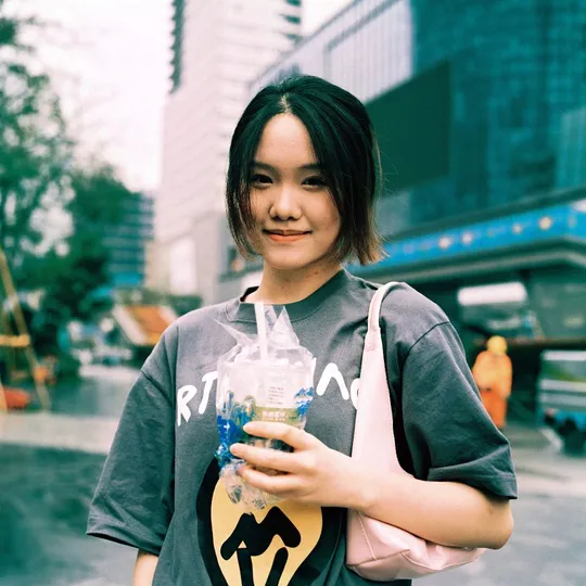 一位年轻女子手持一瓶饮料和塑料袋站在街头