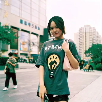 一个穿着印有男孩的T恤衫的女孩站在滑板上 在人行道上。