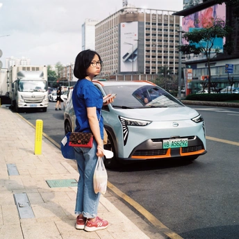一位穿着蓝色衣服的年轻女子站在城市街道的人行道上 一辆车停在路边。